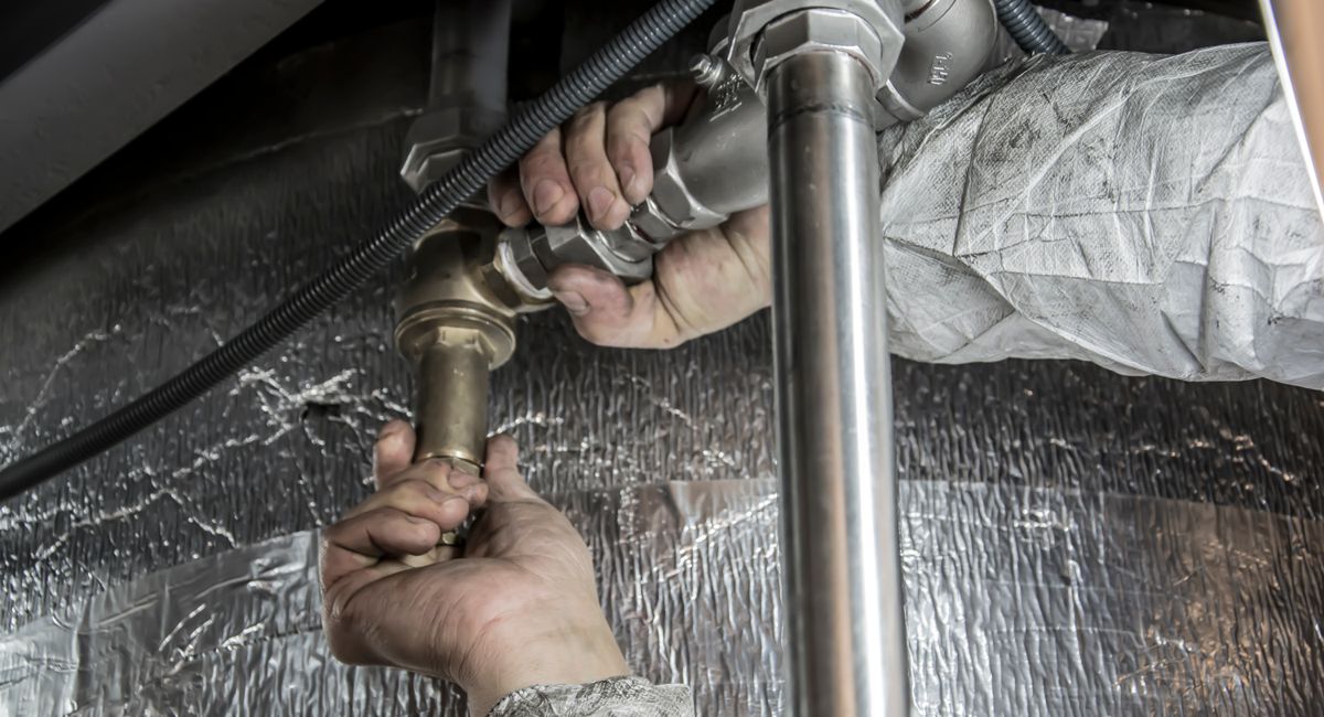 Mains d'un plombier chauffagiste raccordant des tuyaux en acier sur un chantier